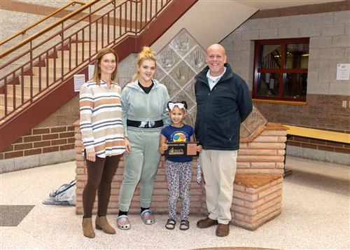 Raydence Poston, Harding's November Stairclimber, poses with her picture, family members and Assistant Principal Yonkers.