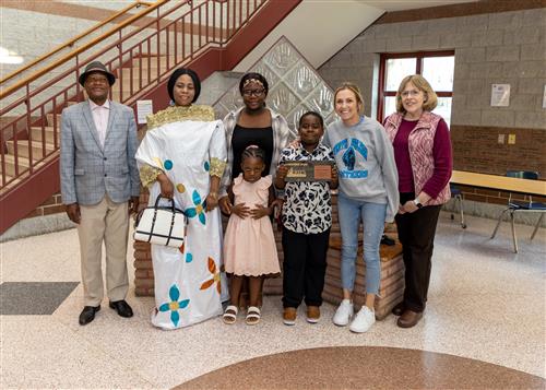 Victoire Mayele, Pfeiffer-Burleigh's May 2023 Stairclimber, poses with his plaque, family members and school staff.