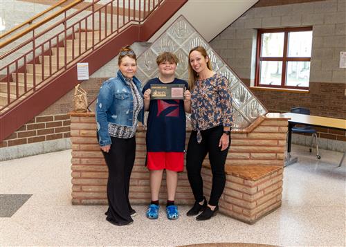 Zane O'Hara, Wilson Middle School's May 2023 Stairclimber, poses with his plaque, family member and school administrator.