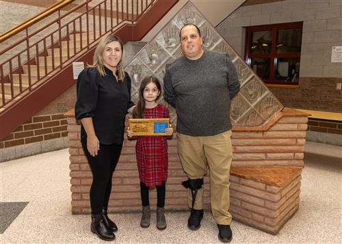 Tara Hoxha, Perry Elementary's Stairclimber for December, posing with her plaque, family member and AP Rick Gudowski.