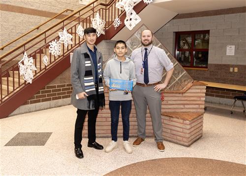 Fawad Ansari, East's January Stairclimber, poses with his plaque, a family member, and Principal Koval.