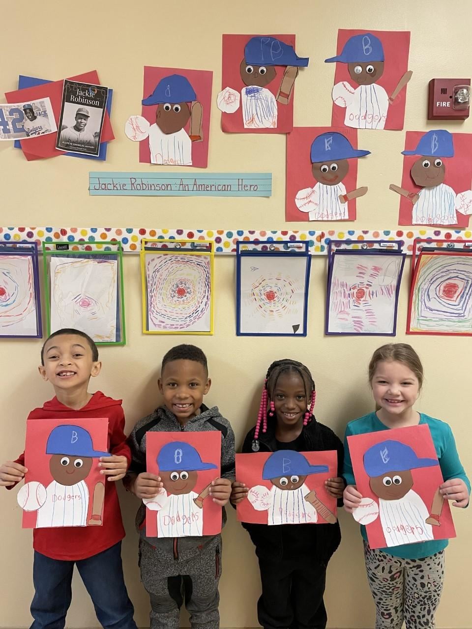 Smiling students lined up against a wall holding construction paper projects with the image of Jackie Robinson.