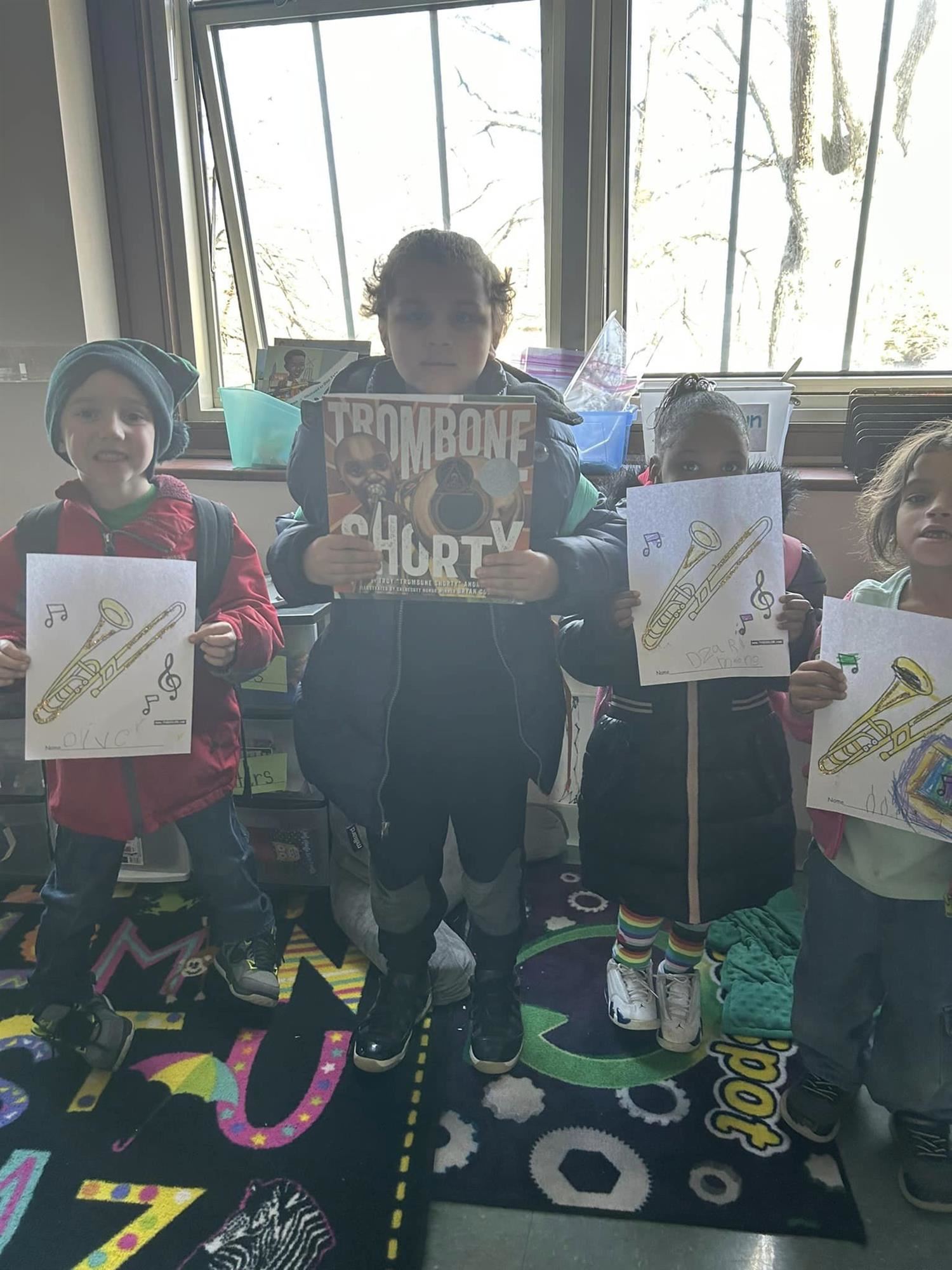 Photo shows four kindergarteners displaying coloring pages of a trombone and also the book "Trombone Shorty."