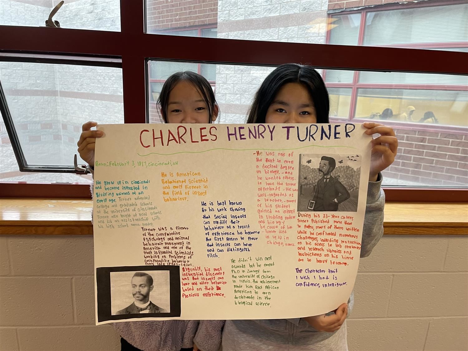 Two female students holding a colorful poster board with information about Charles Henry Turner.