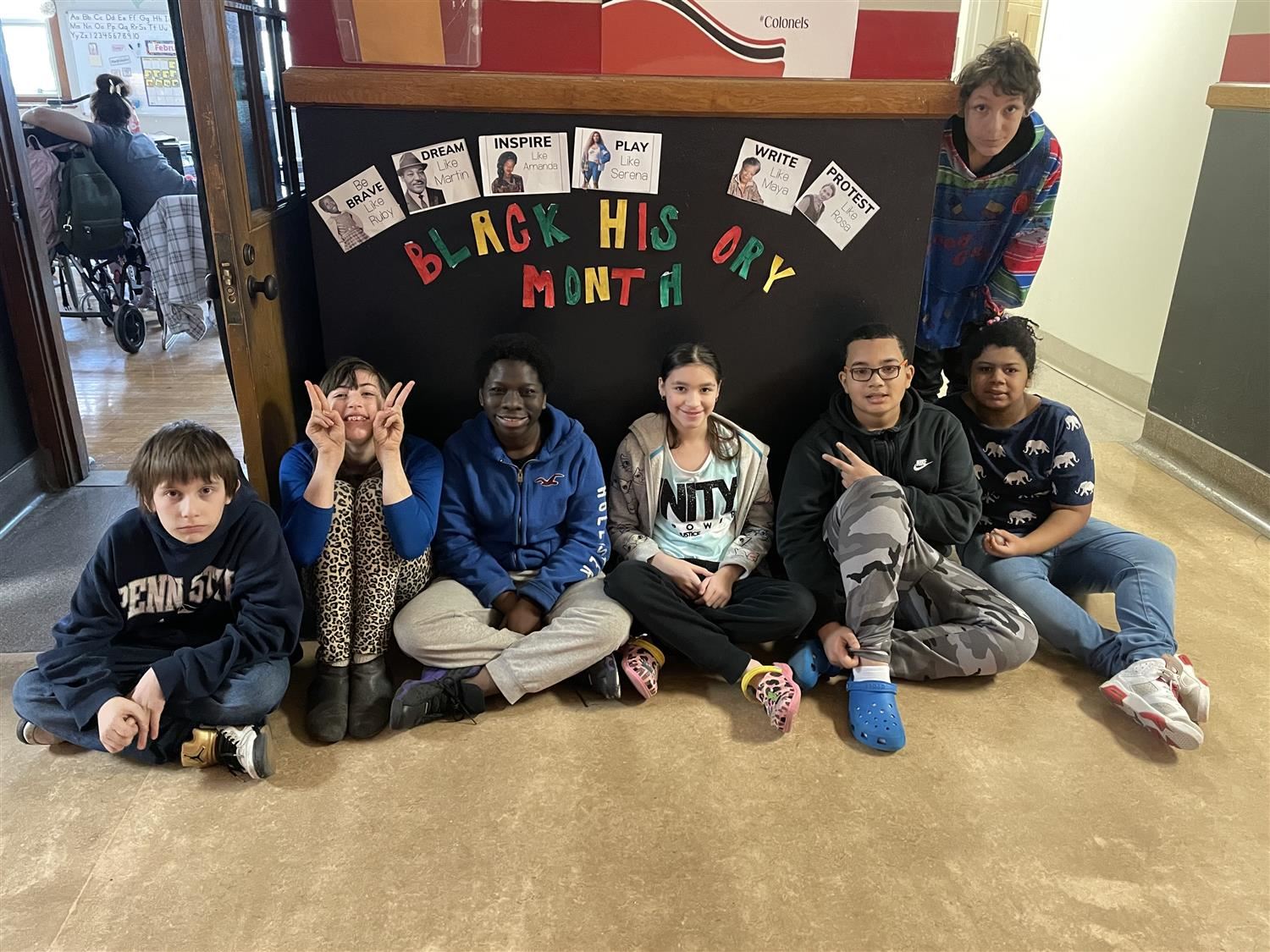 Six students sitting around a bulletin board they designed honoring Ruby Bridges, Amanda Gorman, MLK, Serena Williams, Maya A