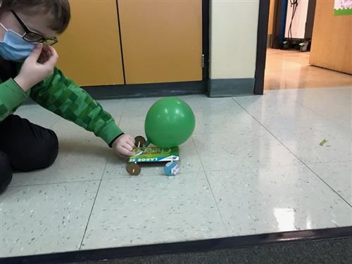 Photo shows a student preparing to race a cardboard car powered by a green balloon.