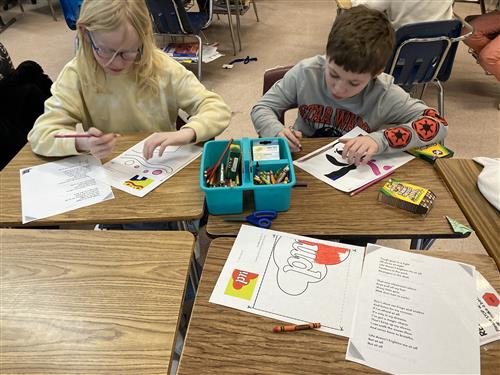 A boy and girl sit at desks, creating artwork that shows a portrait of Maya Angelo and words in a quote.