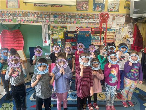 Photo of Grover Cleveland kindergartners holding paper astronaut helmets to their faces.