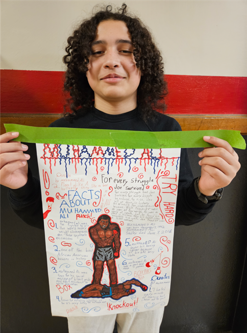 A male student displays a poster with biographical information about Muhammed Ali.