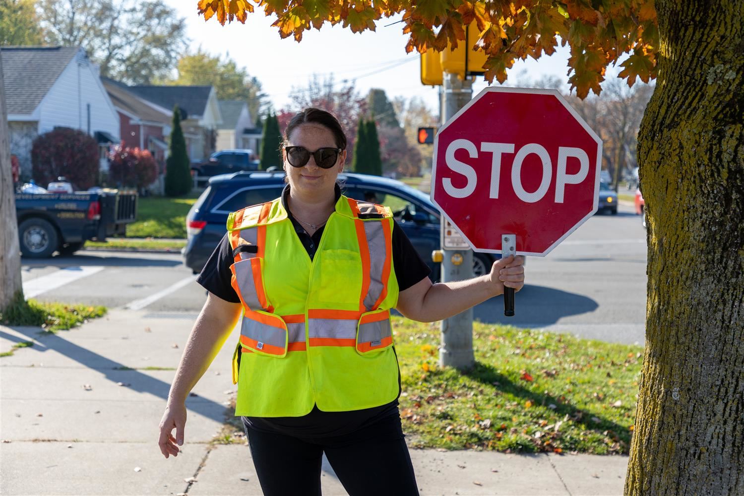 Photo of  a female crossing guard wearing a florescent yellow reflective safety best and holding a "STOP" sign.