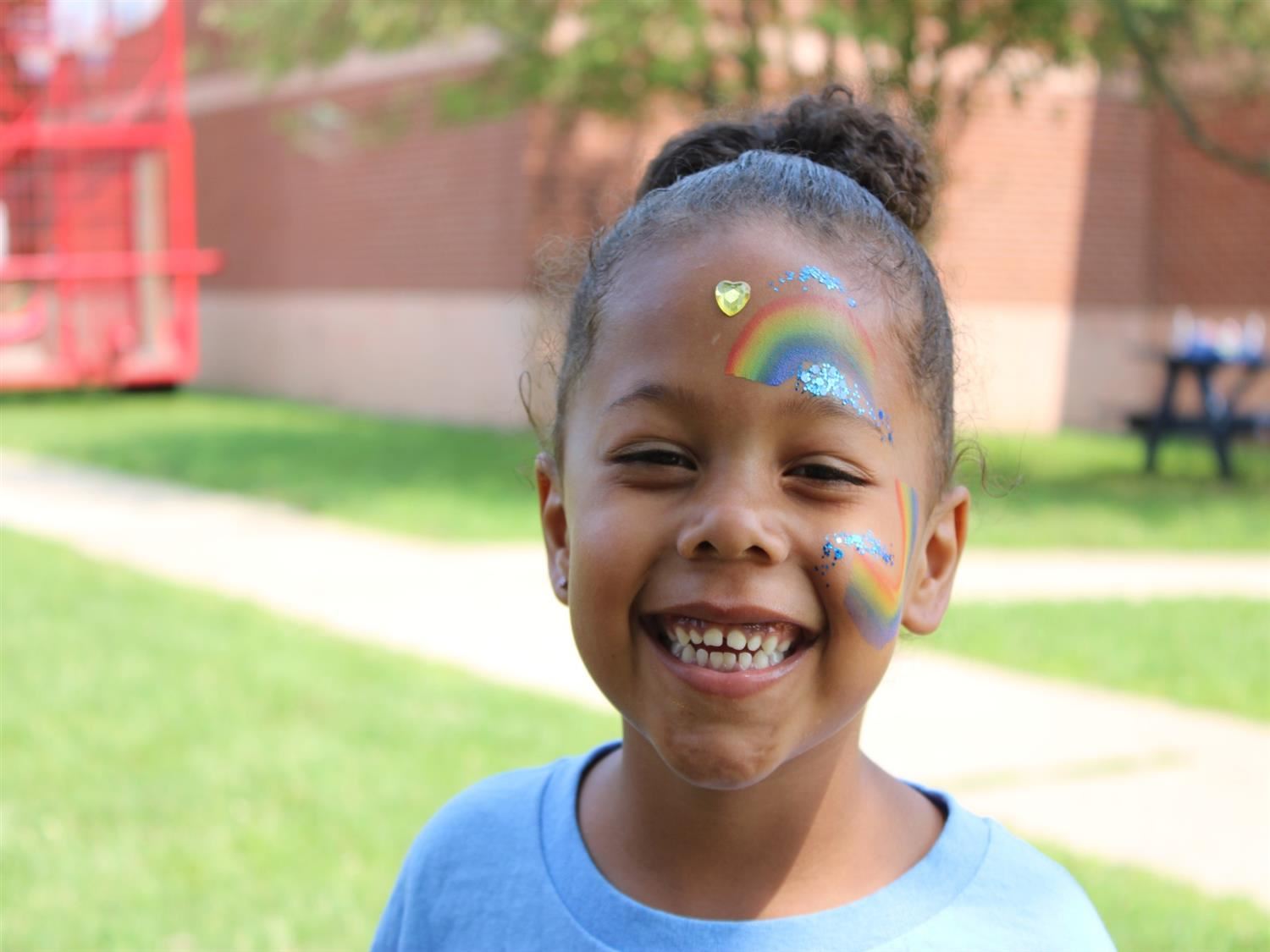 Young girl with rainbows and glitter painted on her smiling face.