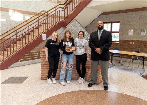 Olivia Boring, Erie High School's May 2023 Stairclimber, poses with her plaque, two other young females, and Ken Nickson.