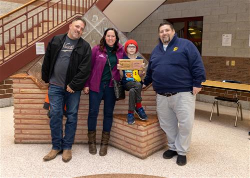 Logan Lindsey, JoAnna Connell's January 2023 Stairclimber, poses with his plaque with family members and Principal Causgrove.